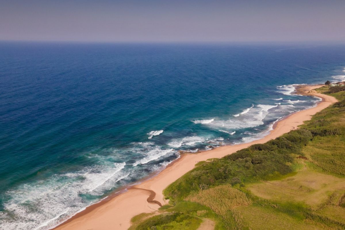 An aerial view of the coastal landscape, showcasing the sandy beach, ocean waves, and surrounding natural vegetation.