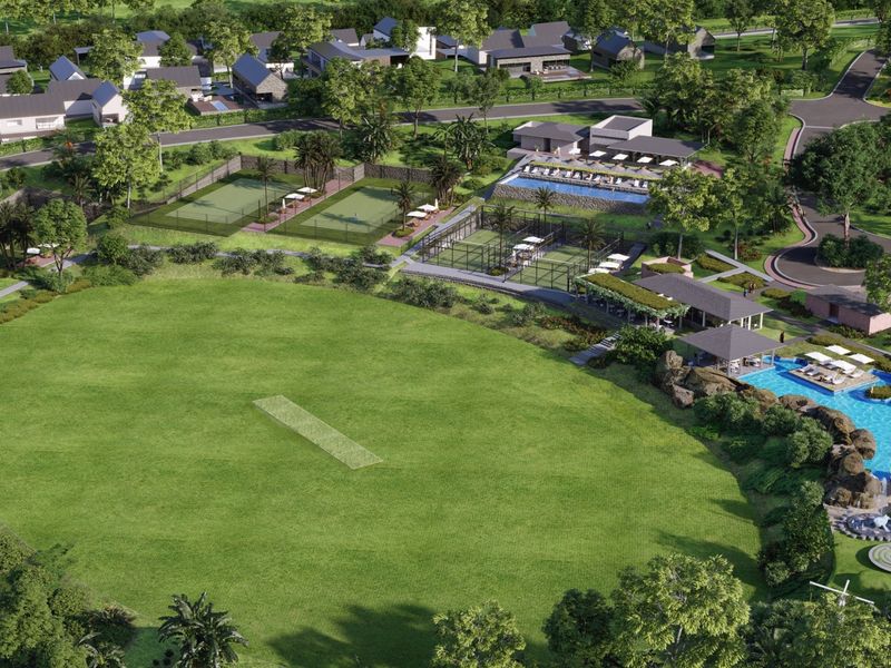 Aerial view of a residential estate featuring a cricket pitch, tennis courts, swimming pool, clubhouse, and landscaped recreational grounds.