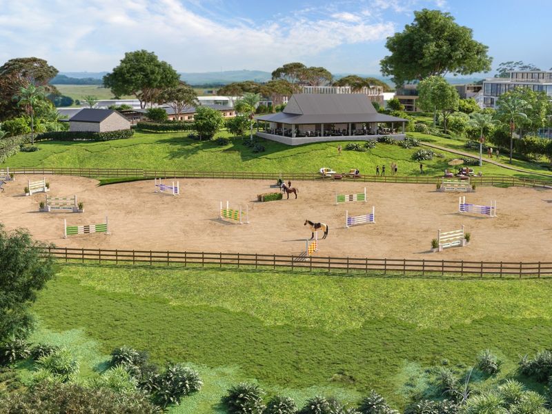 An aerial view of a professional equestrian show jumping arena featuring post and rail fencing and various jumping obstacles set within a landscaped estate.