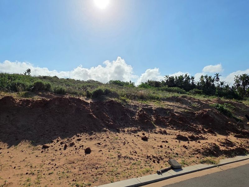 A vacant residential plot featuring an elevated sandy embankment and direct access to a paved street.