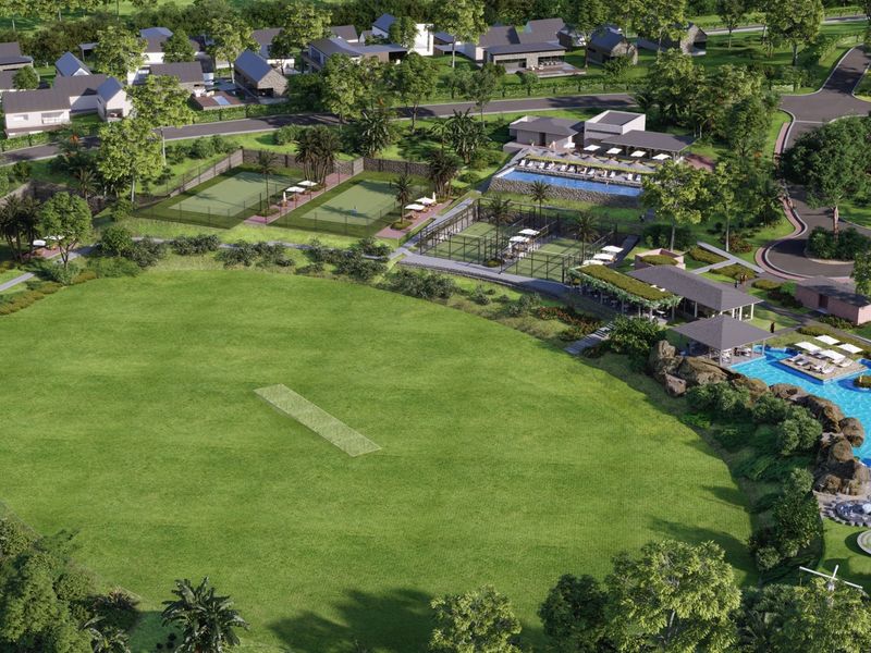 Aerial view of a residential estate featuring a cricket pitch, tennis courts, swimming pool, and clubhouse facilities within a landscaped community setting.