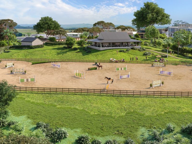 An aerial view of a professional equestrian arena featuring show jumping obstacles, post and rail fencing, and an adjacent clubhouse facility.