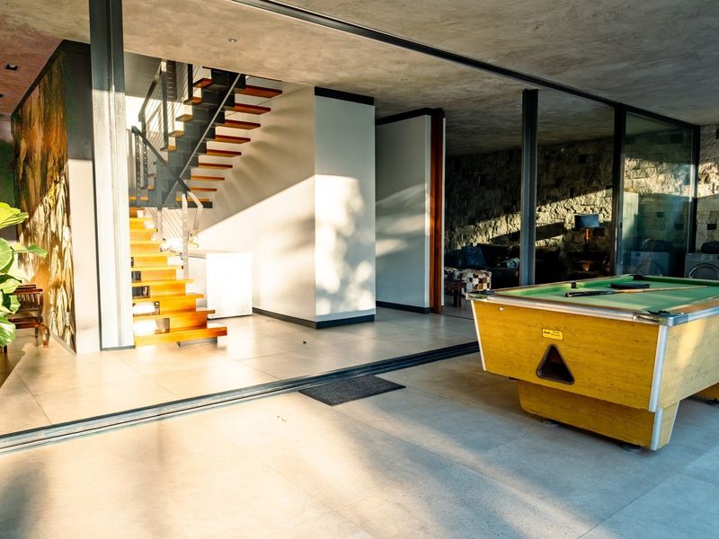 Spacious open-plan living area featuring a modern floating staircase, stone feature wall, and large sliding glass doors opening to the outdoors.