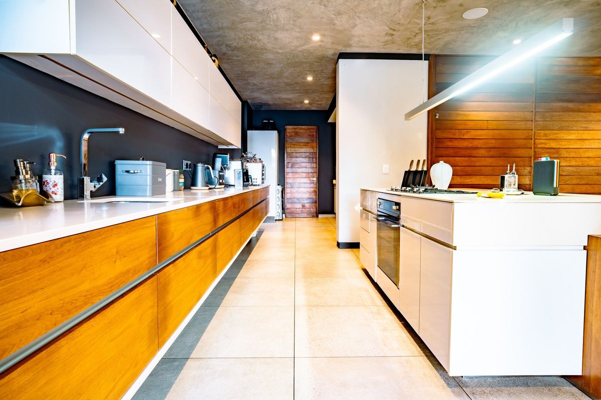 Modern kitchen featuring sleek white and wood cabinetry, a central island with built-in oven, stone countertops, and a contemporary concrete ceiling finish.