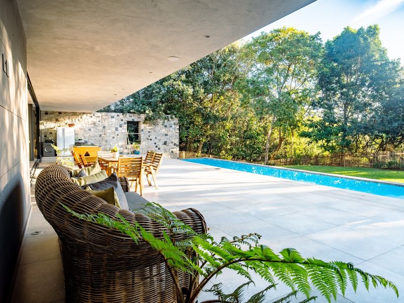 Spacious covered patio featuring large format floor tiles, recessed lighting, and seamless access to a long lap pool and landscaped garden.