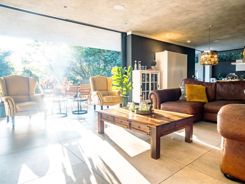 Spacious open-plan living area featuring large format floor tiles, a concrete-finish ceiling, and expansive sliding glass doors that open to an outdoor patio.