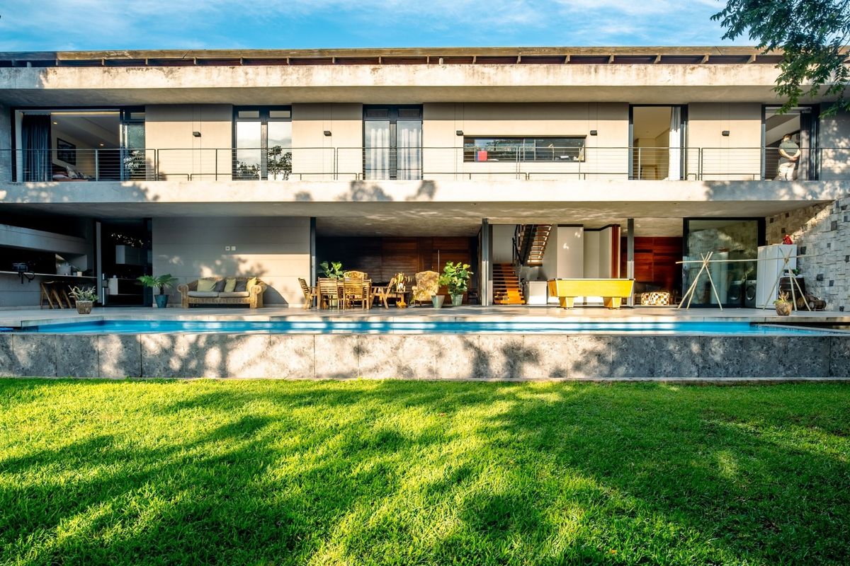 A modern two-story residence featuring a spacious rear patio, swimming pool, stone-clad walls, and a large upper-level balcony overlooking the garden.