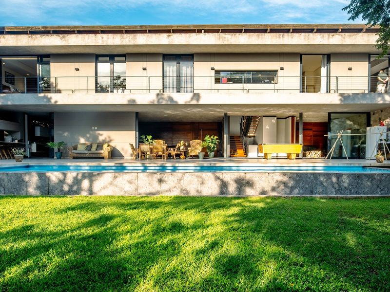 A modern two-story residence featuring a spacious rear patio, swimming pool, stone-clad walls, and a large upper-level balcony overlooking the garden.