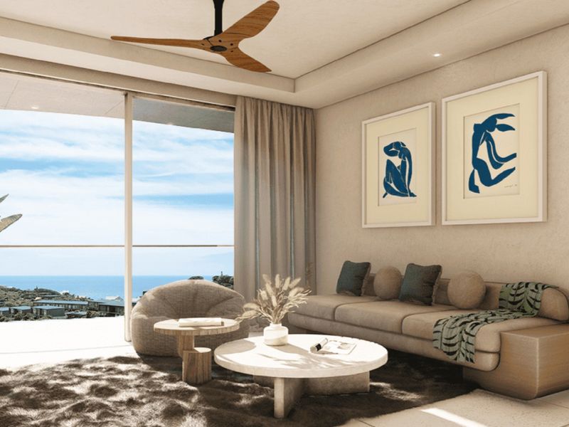A modern living room featuring a ceiling fan, recessed lighting, and large sliding glass doors that open to a scenic coastal view.