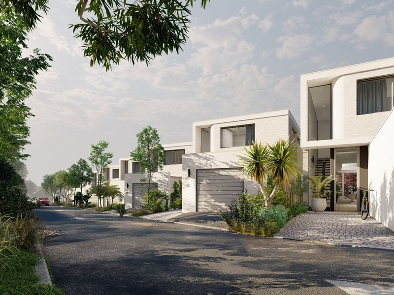 A street-level view of a modern townhouse development featuring clean architectural lines, paved driveways, and integrated garage doors.