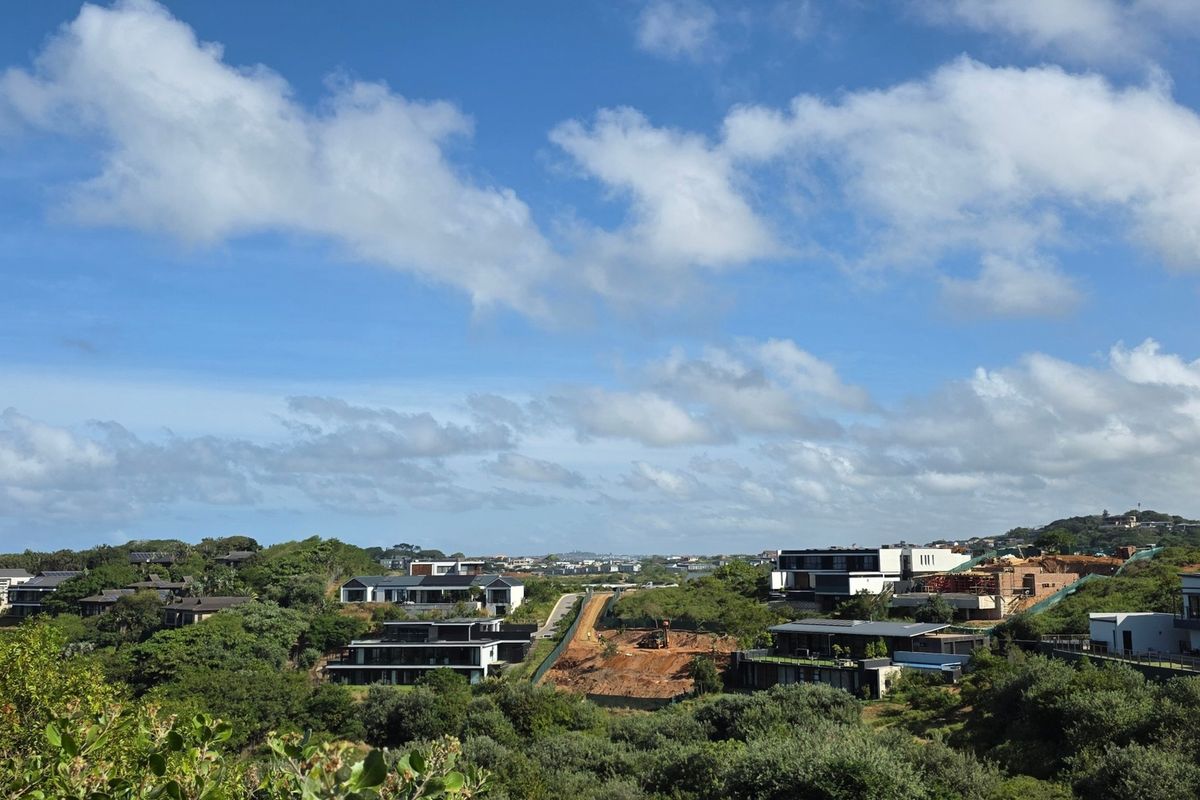 A scenic elevated view overlooking a residential estate with modern homes and surrounding natural vegetation under a clear blue sky.