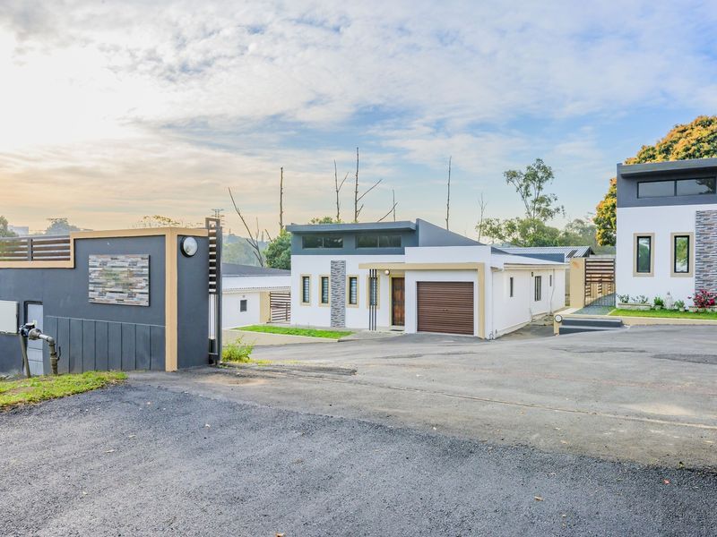Modern apartment complex entrance featuring a paved driveway, secure gated access, and contemporary architectural facade with stone detailing.