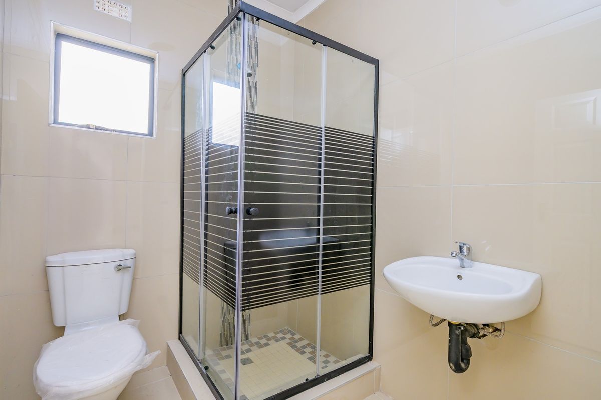 A compact bathroom featuring a glass shower enclosure, wall-mounted basin, and toilet with neutral wall tiling.