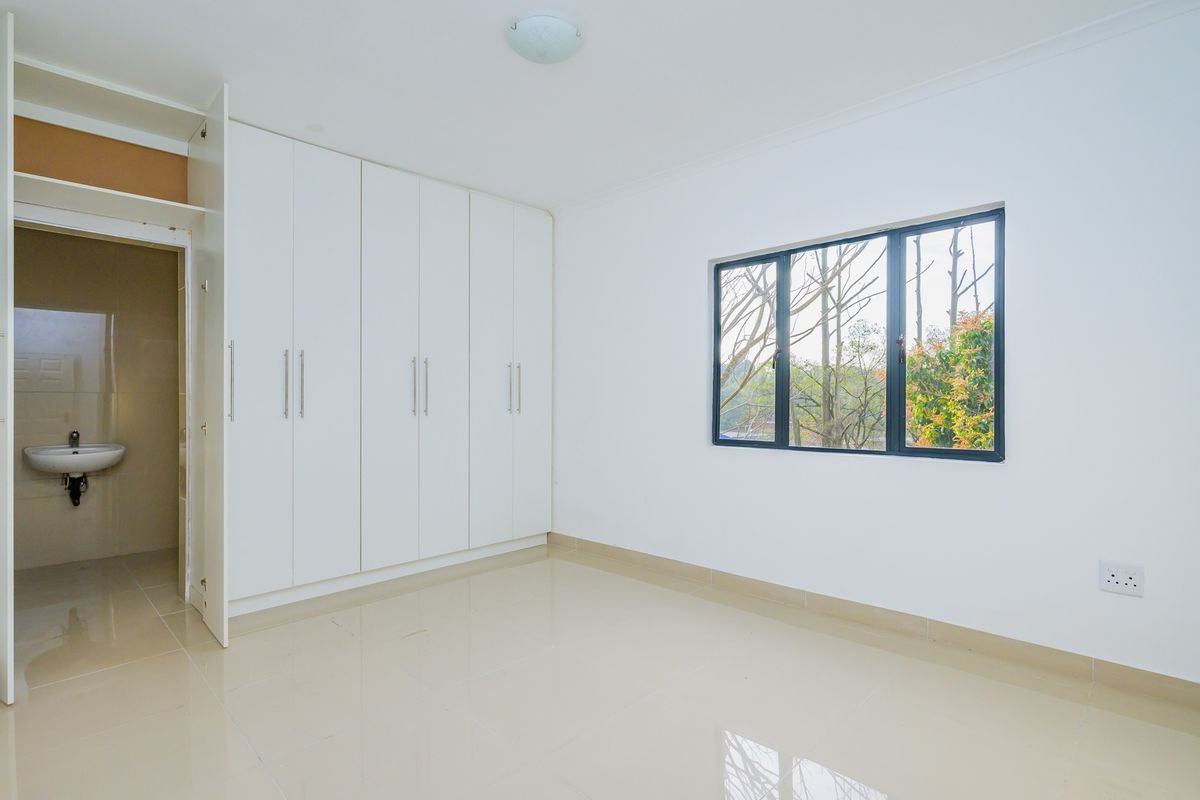 A bright, empty bedroom featuring neutral tiled flooring, ample built-in cupboard space, and an en-suite bathroom, offering a clean and versatile living area.