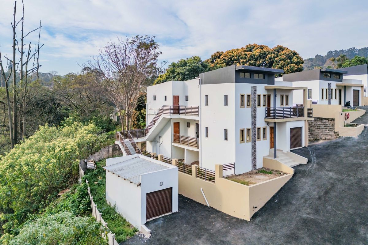Aerial view of a modern multi-level apartment complex featuring external staircases, balconies, and a detached garage structure set against a natural landscape.