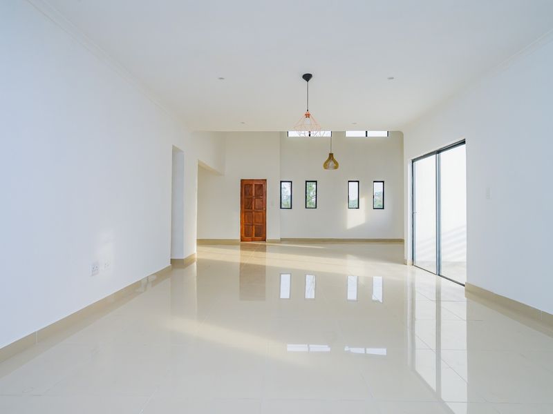 A bright, spacious, and empty living area featuring polished tile floors, modern pendant lighting, and large sliding glass doors leading to the exterior.