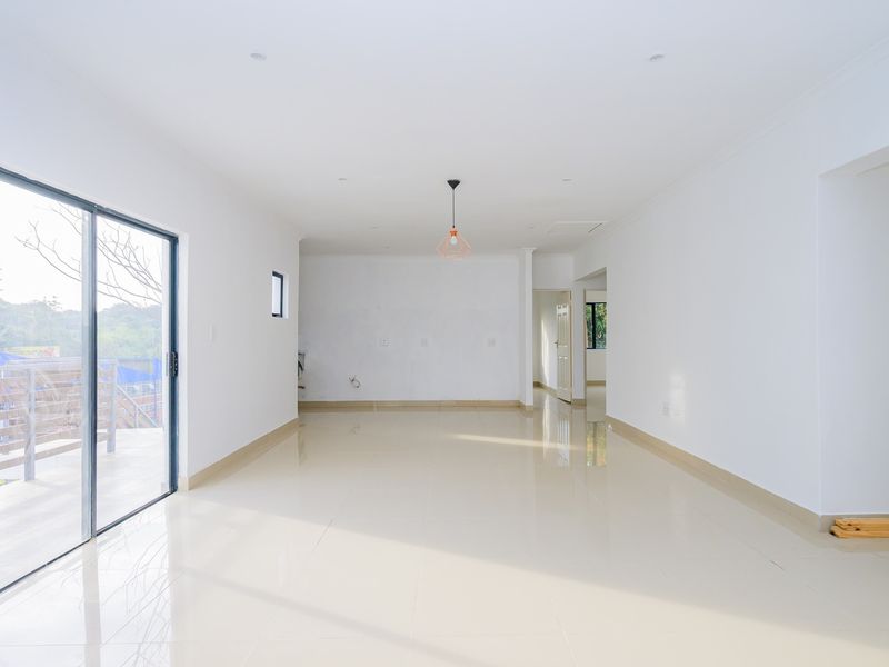 A bright, spacious open-plan living area featuring neutral porcelain tile flooring, recessed lighting, and a large sliding glass door leading to an outdoor space.