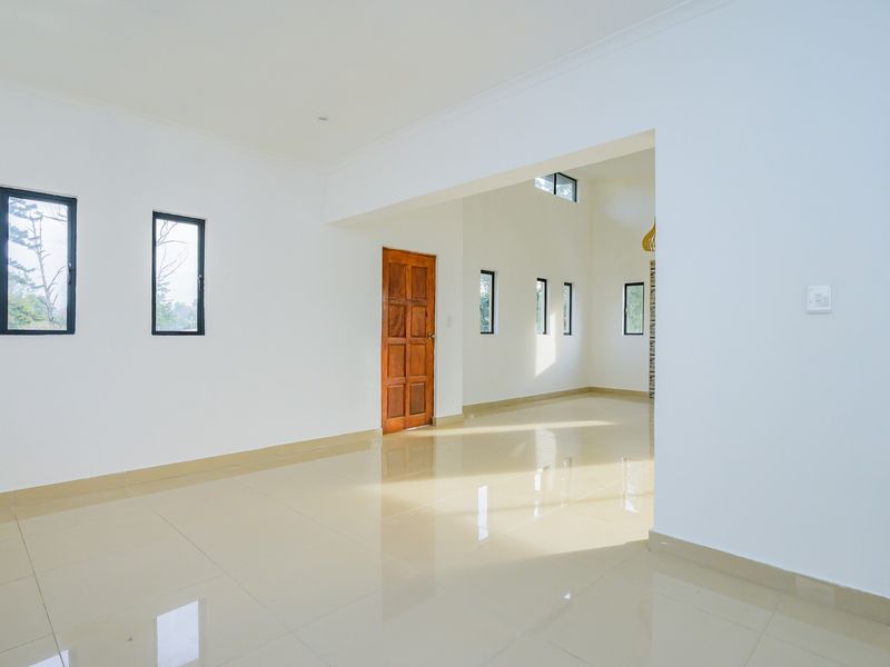 Spacious open-plan living area featuring neutral tiled flooring, clean white walls, and natural light through multiple aluminium-framed windows.
