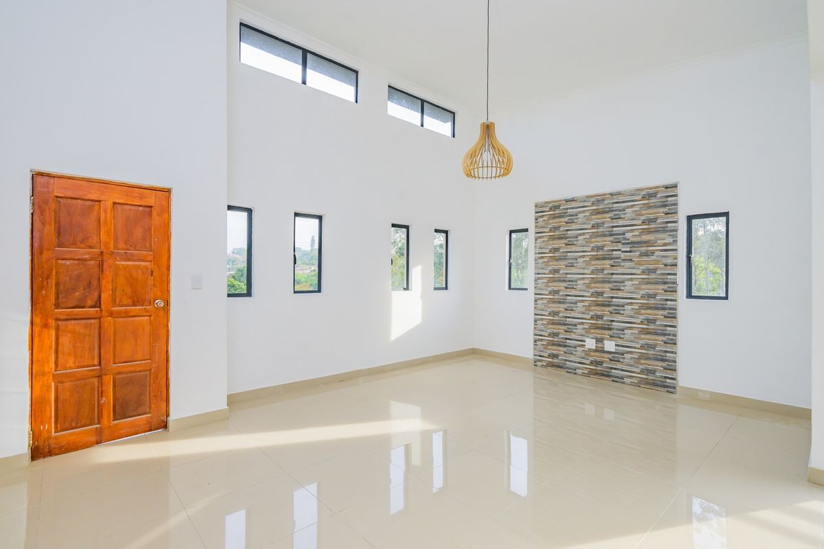 Spacious, light-filled living area featuring high ceilings, polished tile flooring, and a decorative stone feature wall.