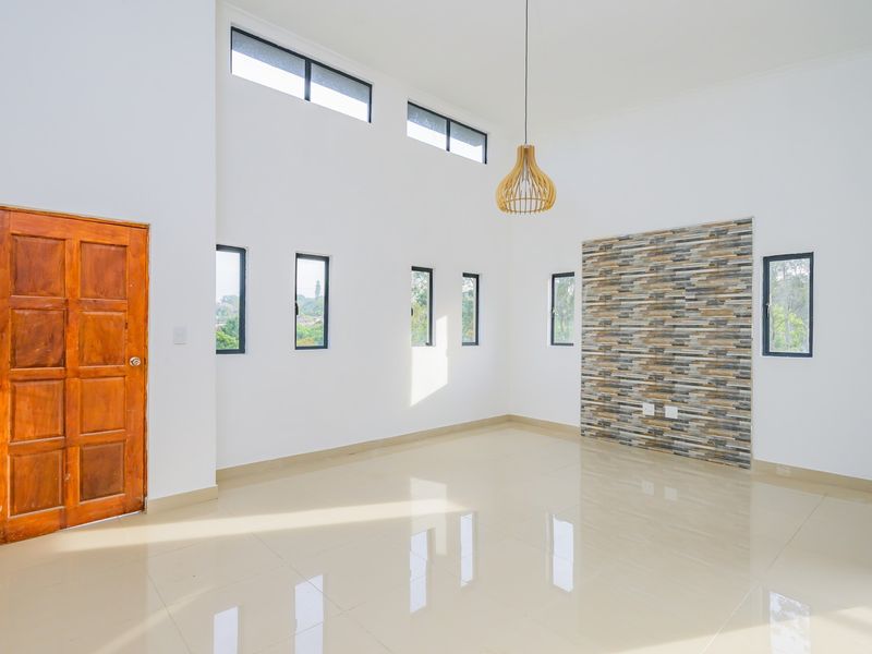 Spacious, light-filled living area featuring high ceilings, polished tile flooring, and a decorative stone feature wall.