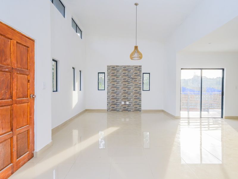 Spacious, light-filled living area featuring polished tile floors, a decorative stone veneer feature wall, and access to an outdoor balcony through sliding glass doors.