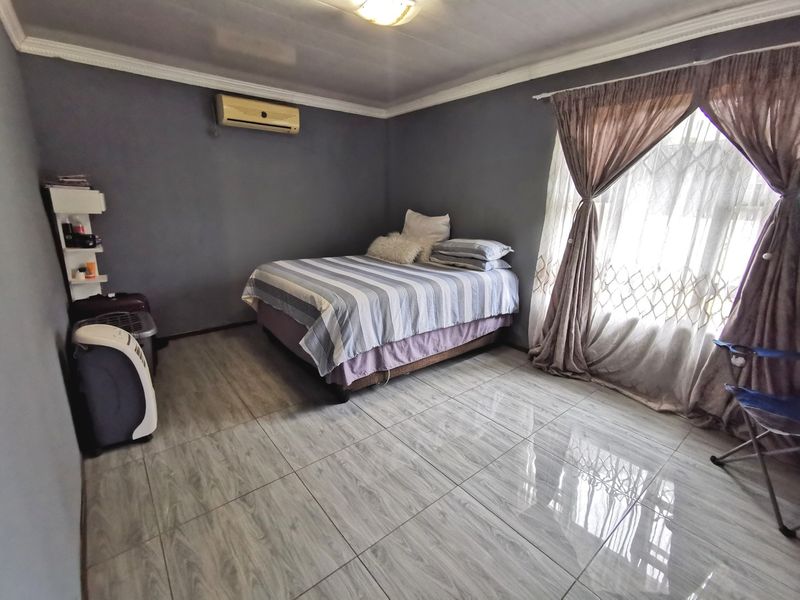 A bedroom featuring tiled flooring, a wall-mounted air conditioning unit, and decorative ceiling cornicing, providing a functional and neutral living space.