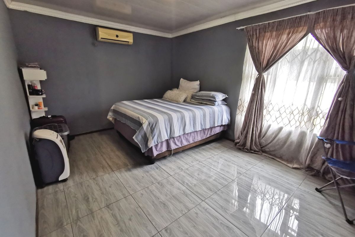 A bedroom featuring tiled flooring, a wall-mounted air conditioning unit, and decorative ceiling cornicing, providing a functional and neutral living space.