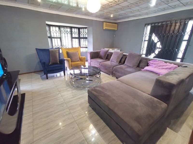 Spacious living room featuring tiled flooring, decorative ceiling tiles, and security gates on windows, providing a functional and comfortable lounge area.