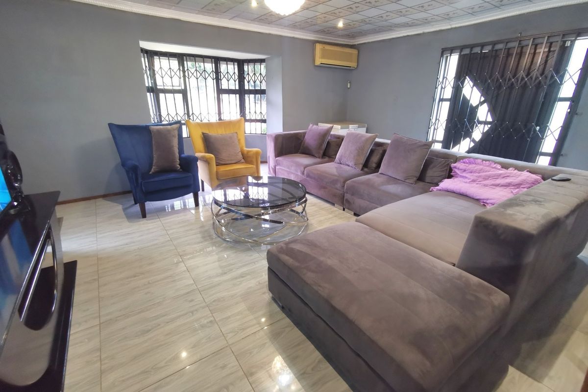 Spacious living room featuring tiled flooring, decorative ceiling tiles, and security gates on windows, providing a functional and comfortable lounge area.