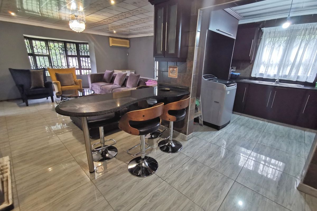 Open-plan living and kitchen area featuring tiled flooring, dark wood cabinetry, a granite breakfast bar, and security bars on the windows.