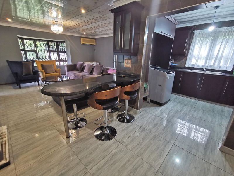 Open-plan living and kitchen area featuring tiled flooring, dark wood cabinetry, a granite breakfast bar, and security bars on the windows.