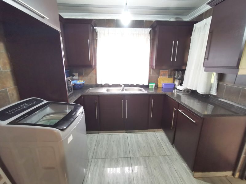 A functional kitchen featuring dark wood cabinetry, granite countertops, a double basin sink, and tiled finishes throughout.