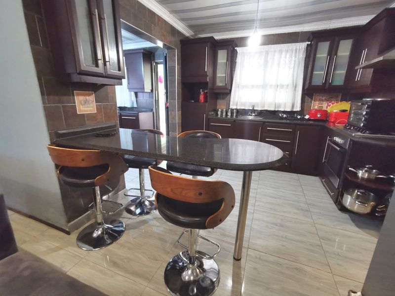 A functional kitchen featuring dark wood cabinetry, granite countertops, a breakfast bar, and tiled finishes, with an adjacent scullery area visible.