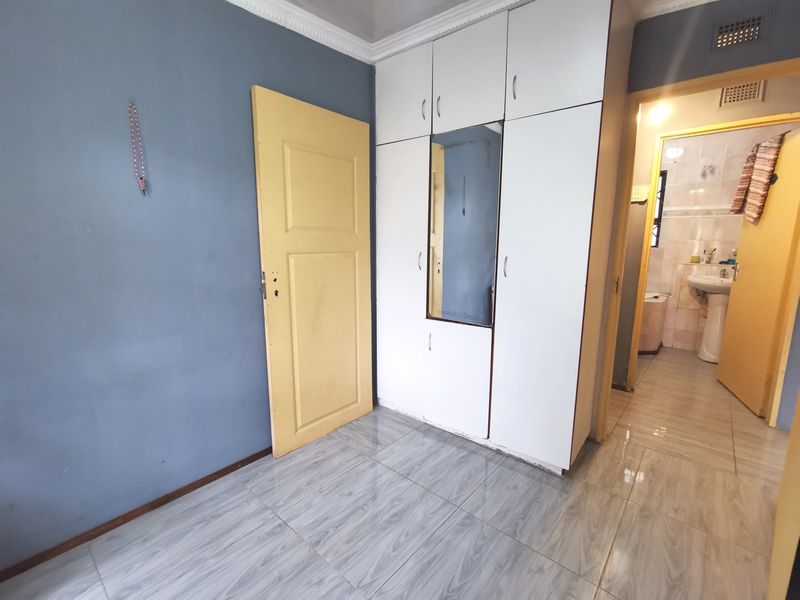 A bedroom featuring tiled flooring, built-in wardrobes with a central mirror, and direct access to an adjacent bathroom.
