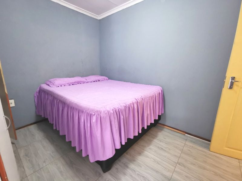 A simple bedroom featuring tiled flooring and neutral grey walls, offering a functional space ready for personalization.
