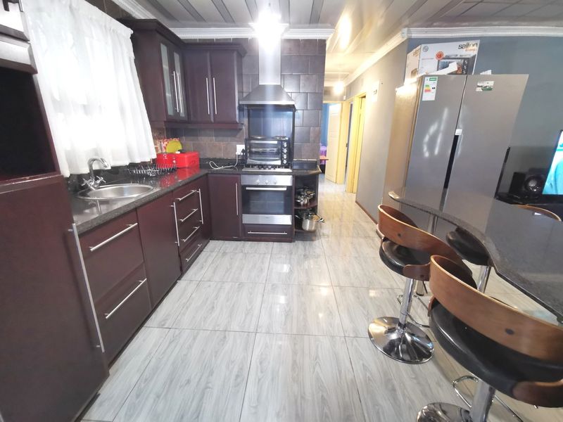 A functional kitchen featuring dark wood cabinetry, granite countertops, stainless steel appliances, and a breakfast bar, finished with modern tiled flooring.