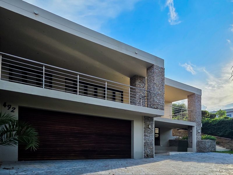 Modern multi-level residence featuring stone cladding, a spacious covered balcony with stainless steel balustrades, and a large timber garage door.