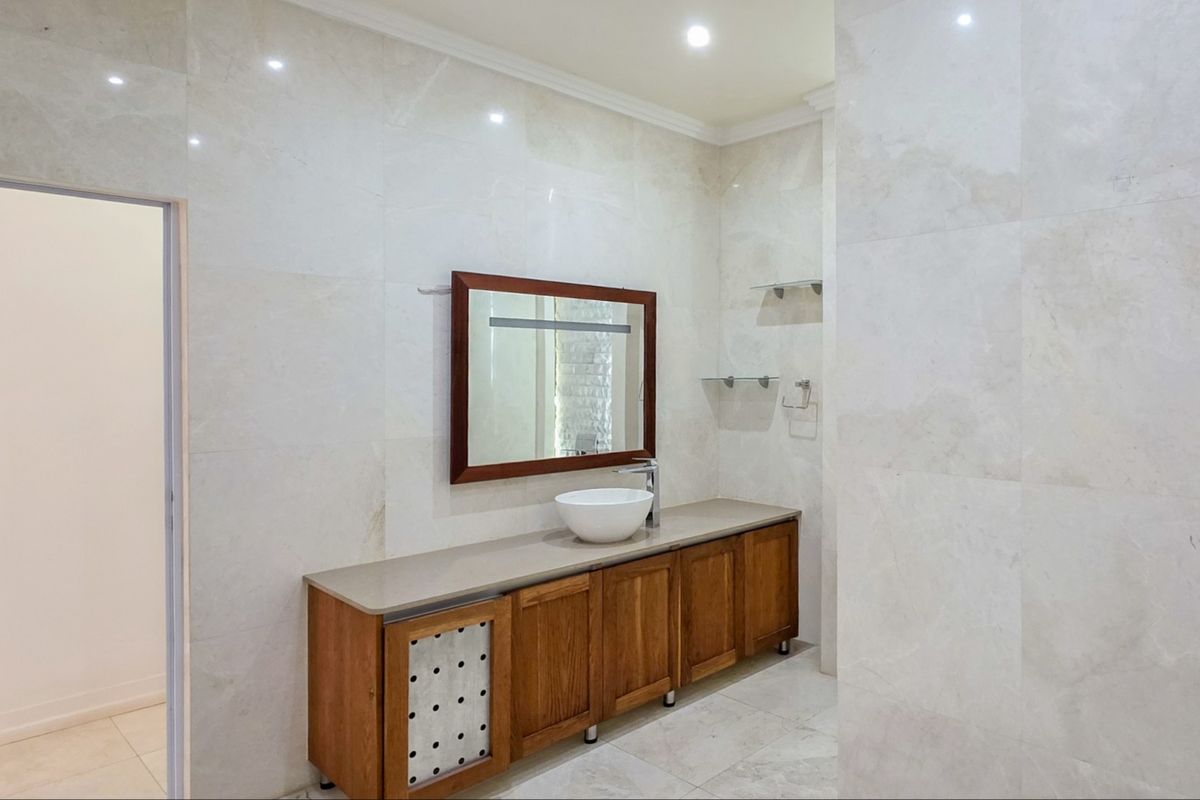 A modern bathroom featuring a wooden vanity cabinet with a vessel sink, marble wall and floor tiles, and a framed wall mirror.