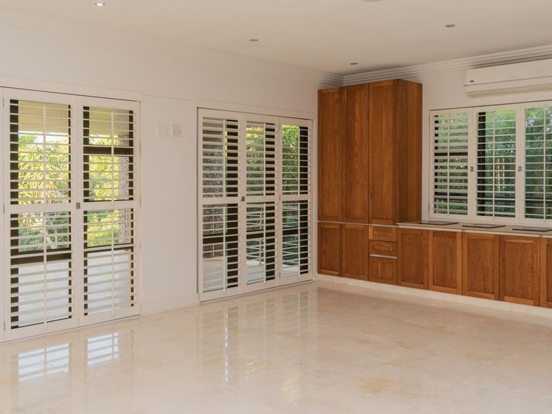 Spacious living area featuring polished stone flooring, built-in wooden cabinetry, and plantation shutters, offering a bright and well-maintained interior space.
