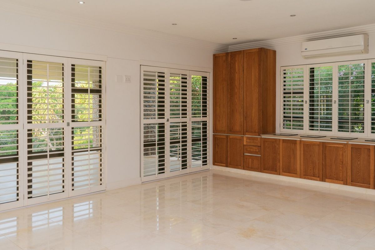 Spacious living area featuring polished stone flooring, built-in wooden cabinetry, and plantation shutters, offering a bright and well-maintained interior space.