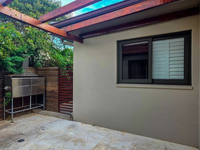A well-maintained outdoor patio area featuring a timber pergola, built-in stainless steel braai, and tiled flooring, perfect for outdoor entertaining.