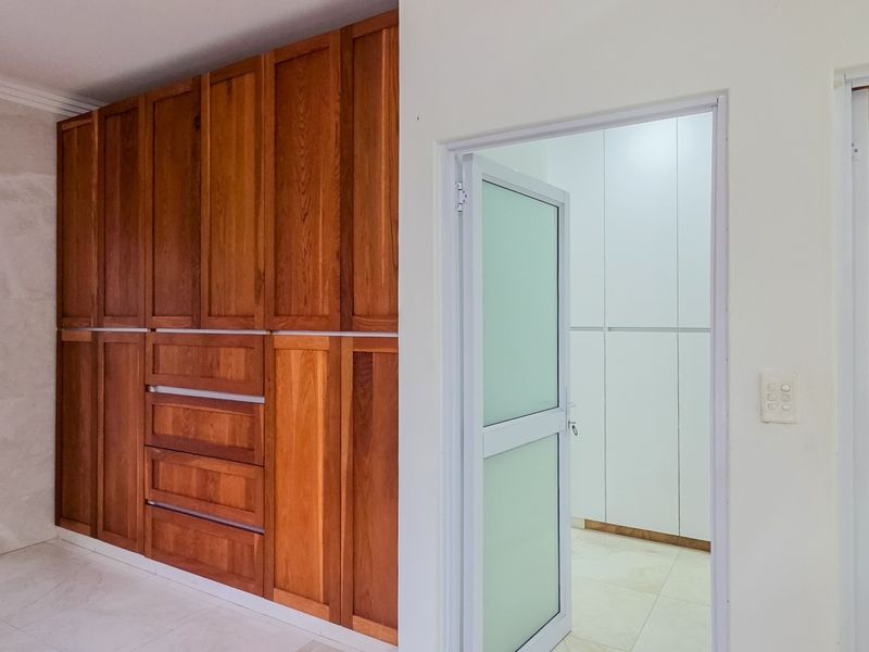 Spacious bedroom area featuring extensive built-in wooden cabinetry, tiled flooring, and a separate walk-in closet or storage space with built-in shelving.