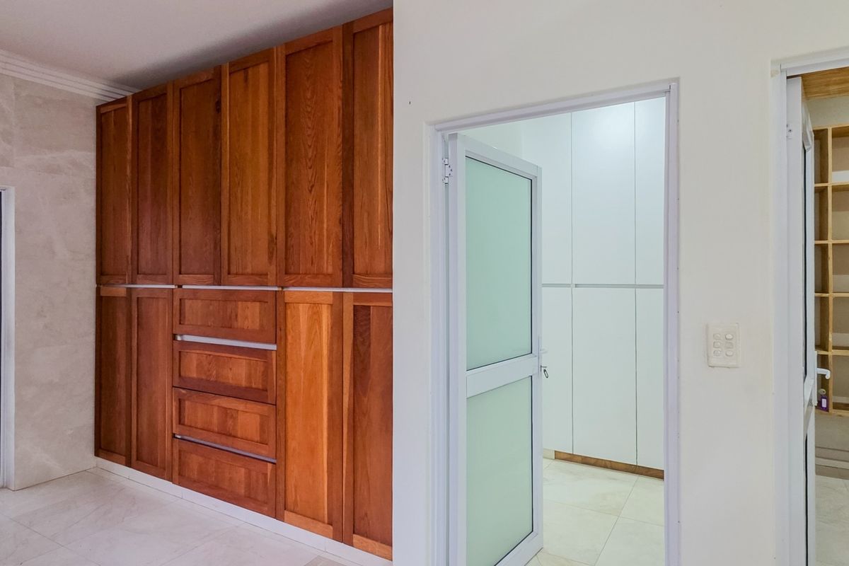 Spacious bedroom area featuring extensive built-in wooden cabinetry, tiled flooring, and a separate walk-in closet or storage space with built-in shelving.