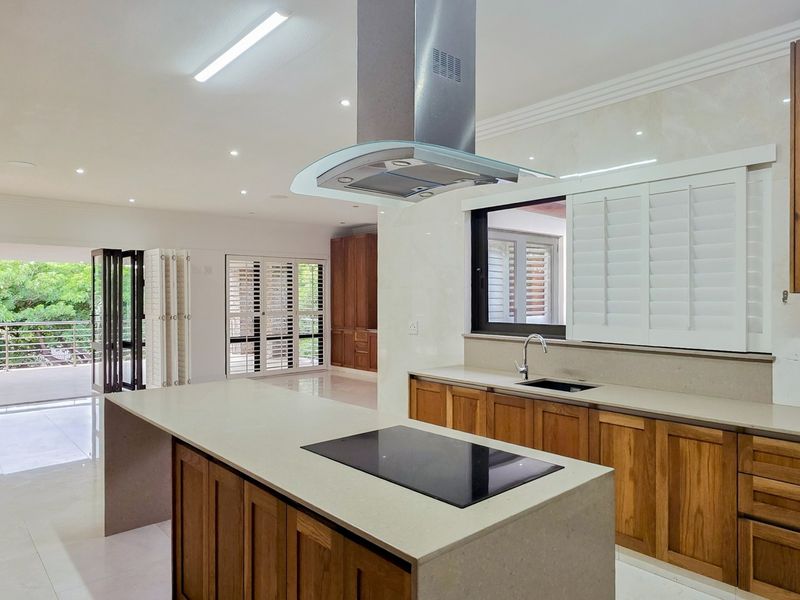 Spacious open-plan kitchen featuring a large island with built-in hob, stone countertops, wooden cabinetry, and seamless flow to an outdoor patio area.