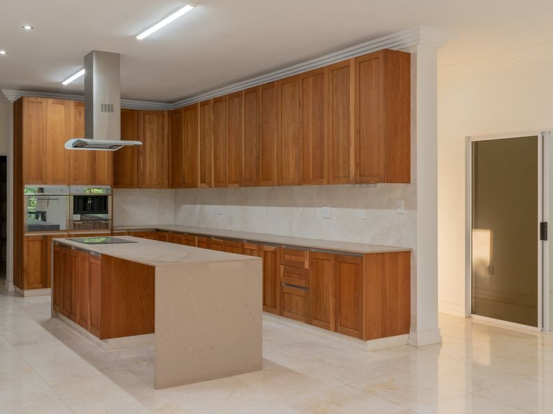 Spacious kitchen featuring extensive wooden cabinetry, stone countertops, a central island, and integrated appliances, finished with neutral tiled flooring and modern recessed lighting.