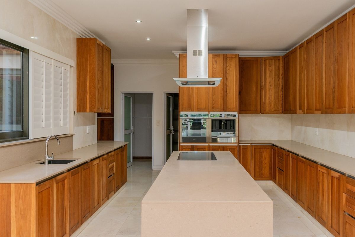 Spacious kitchen featuring extensive wooden cabinetry, a large central island with stone countertops, integrated appliances, and modern recessed lighting.