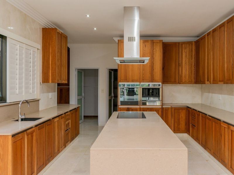 Spacious kitchen featuring extensive wooden cabinetry, a large central island with stone countertops, integrated appliances, and modern recessed lighting.