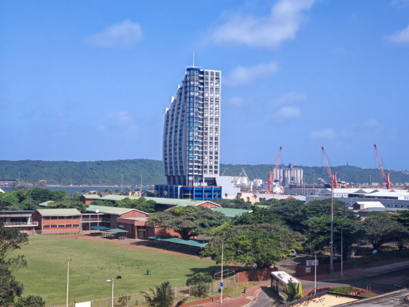 An elevated view of the surrounding urban landscape, featuring a prominent high-rise building and nearby harbour industrial area.