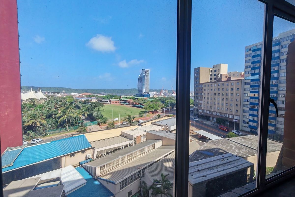 An elevated urban view looking out over the surrounding city buildings, rooftops, and green spaces through a large window.