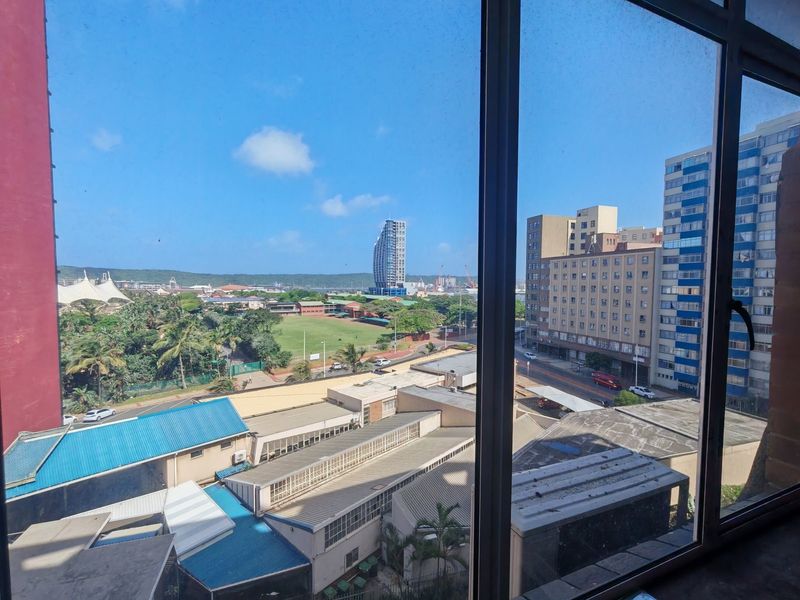 An elevated urban view looking out over the surrounding city buildings, rooftops, and green spaces through a large window.